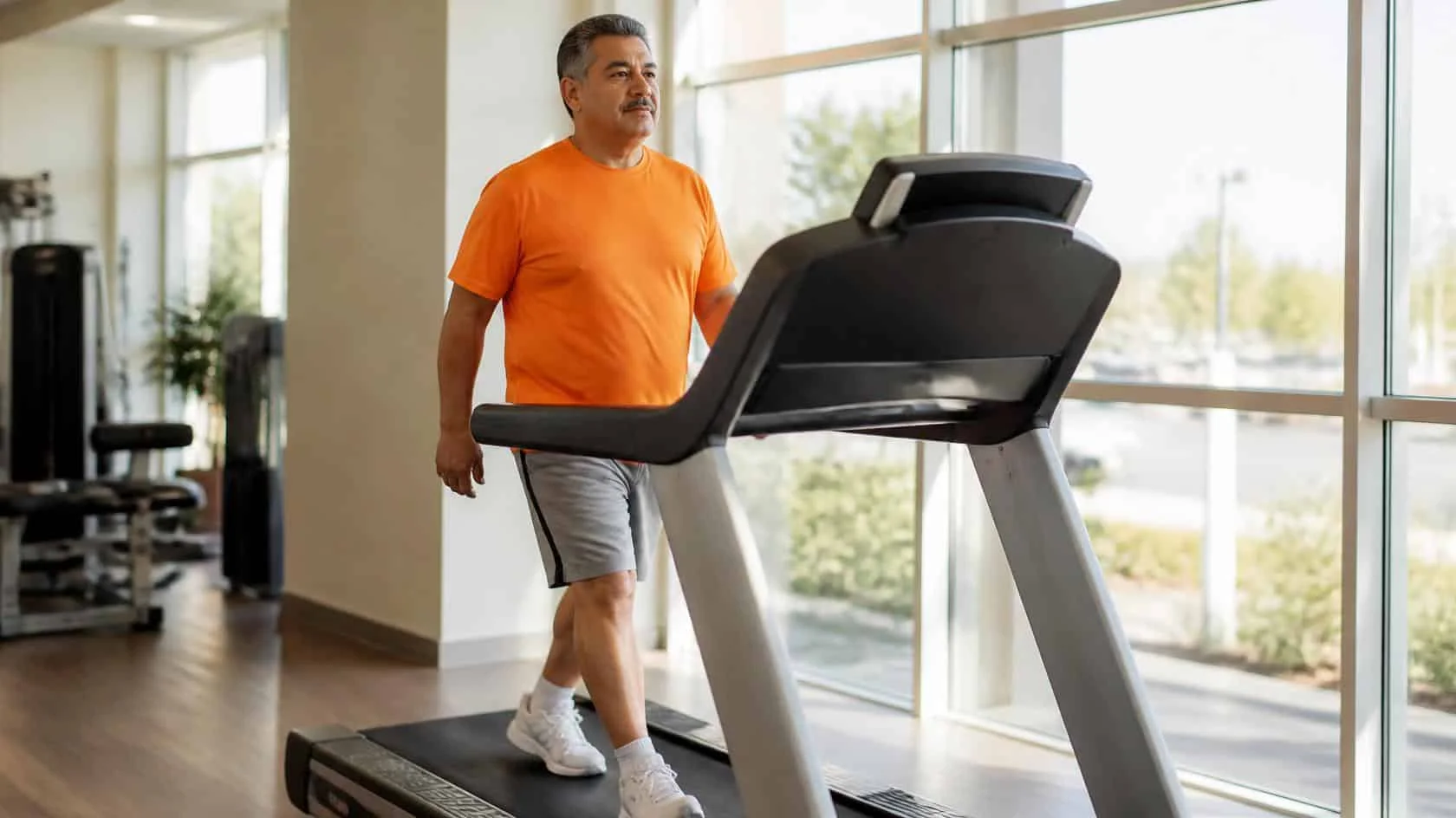 Man in his early 60s walking on a treadmill in a bright fitness room
